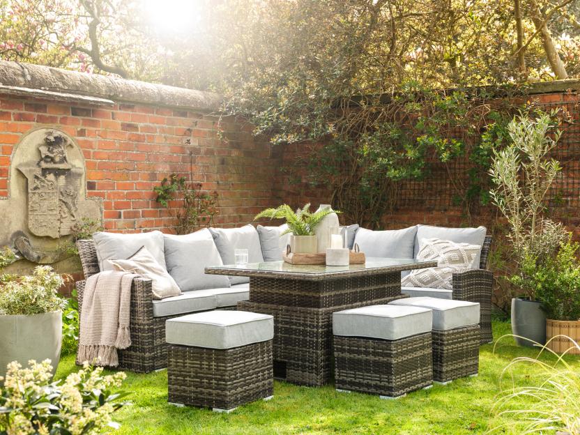 Woven outdoor patio furniture with light grey cushions and matching ottomans on a bright green lawn.
