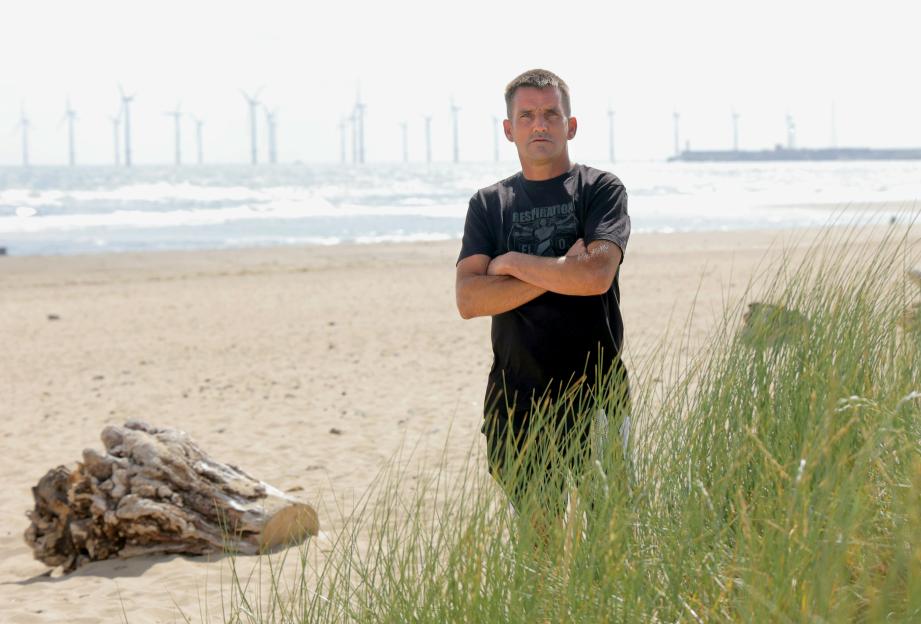 Davey Short, a hero from Seaton Carew, stands on a beach, with the sea and windmills in the background.