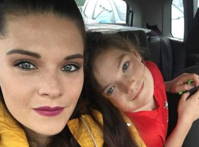 A woman with dark hair and a child in a red shirt posing for a photo.