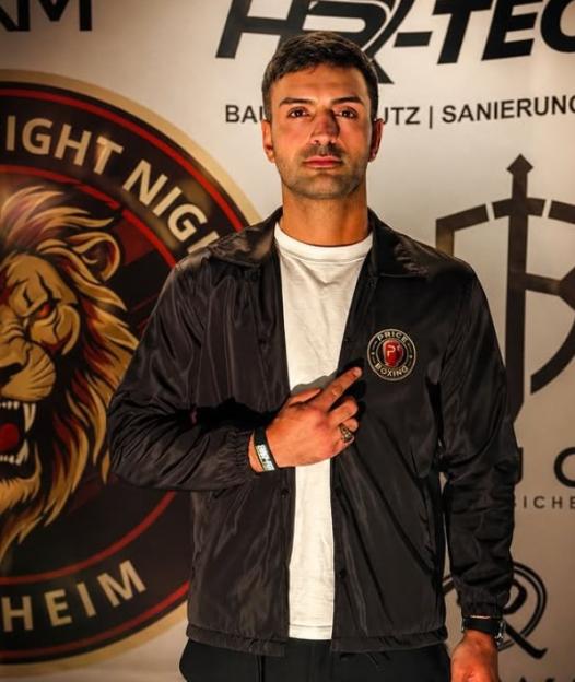 Man wearing a black jacket with a "Price Boxing" patch pointing to his chest.