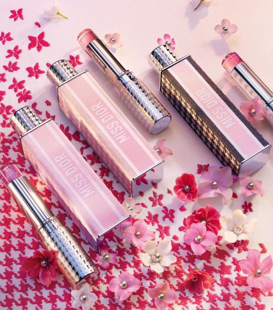 Four Miss Dior lipsticks and their cases surrounded by pink and white flowers.