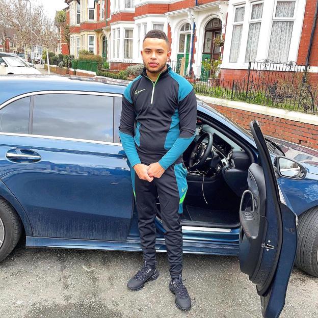 Rafel Jeanne standing in front of a blue car.