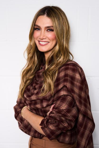Delta Goodrem in a brown plaid shirt, smiling at the camera.