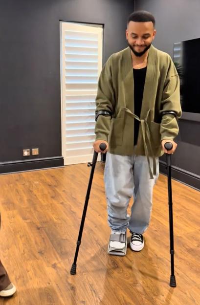 Aston Merrygold using crutches and wearing a medical boot on his right foot.