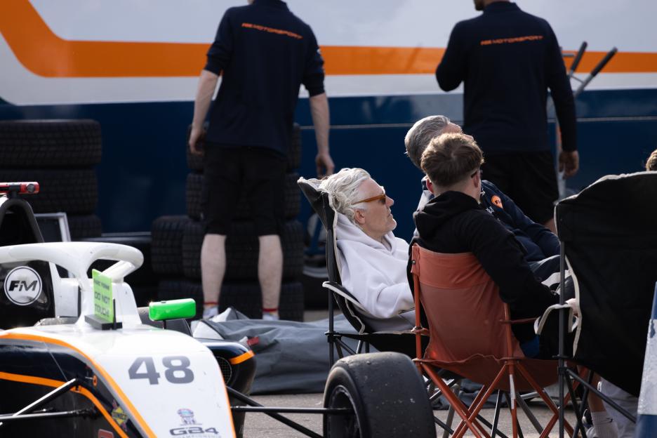 People relaxing at a motorsports event with a race car in the foreground.