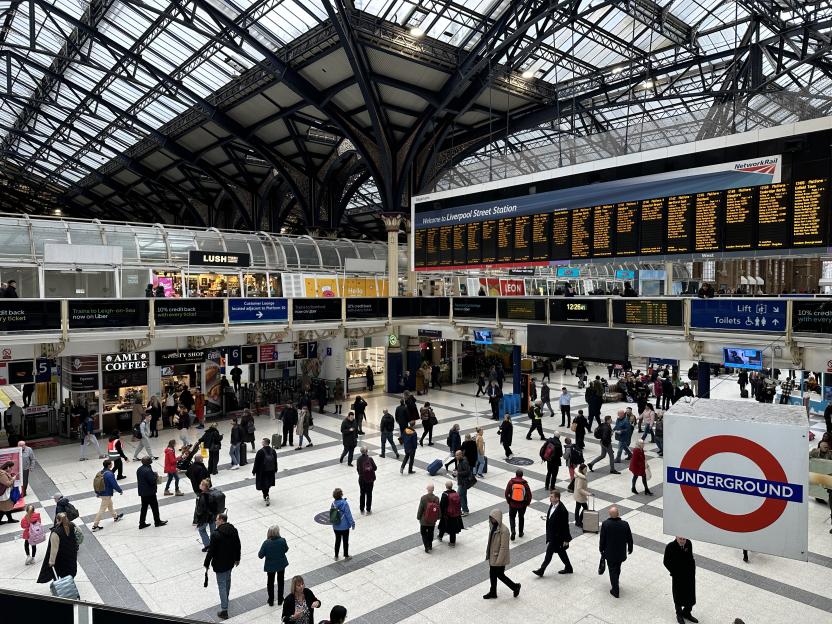 Crowded Liverpool Street station with a large departure board above and London Underground sign.