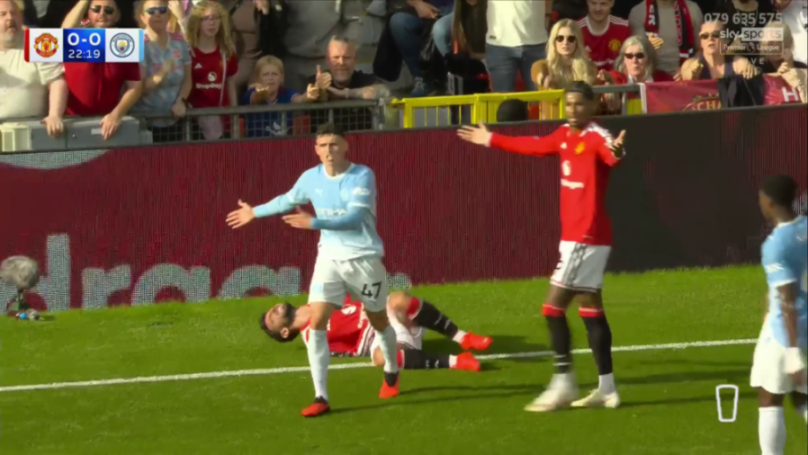 Manchester United and Manchester City players on a soccer field, with a Manchester United player on the ground.