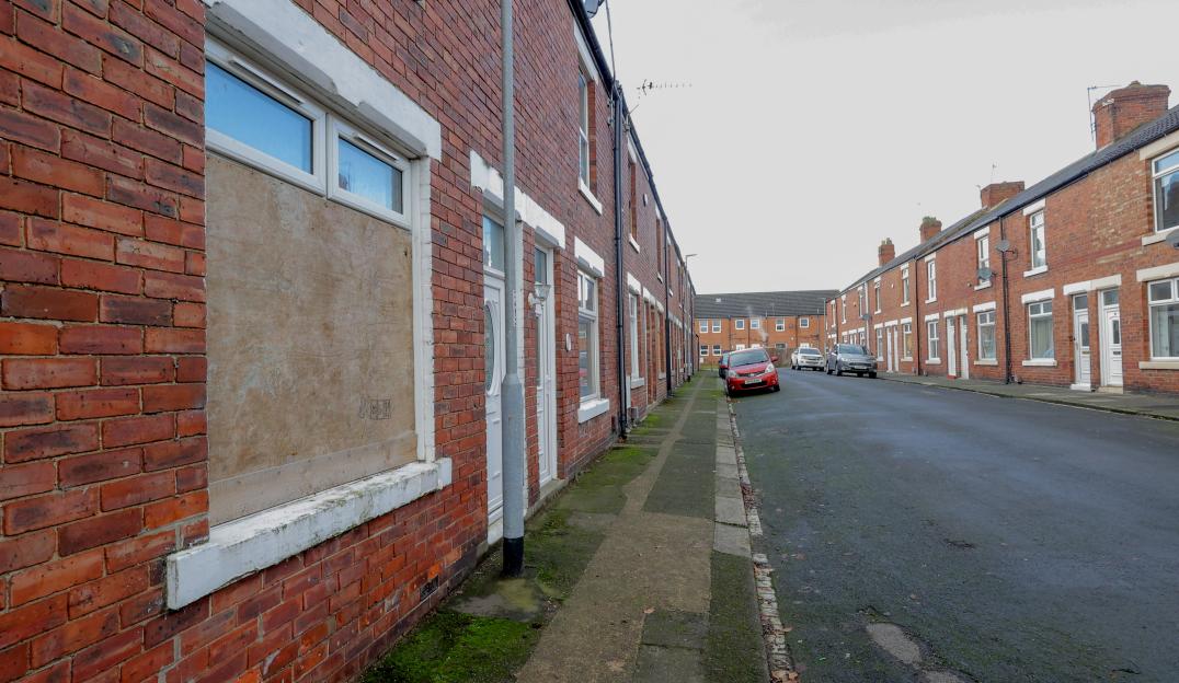 Street in Shildon Town, Co Durham, with boarded-up windows on brick houses and parked cars.