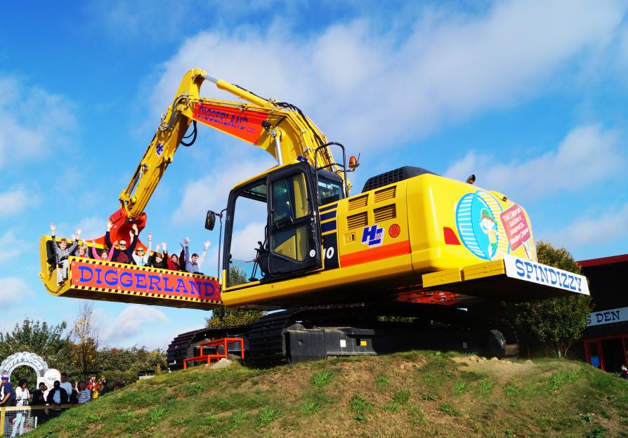 People riding an excavator ride named Spindizzy at Diggerland, with arms raised.