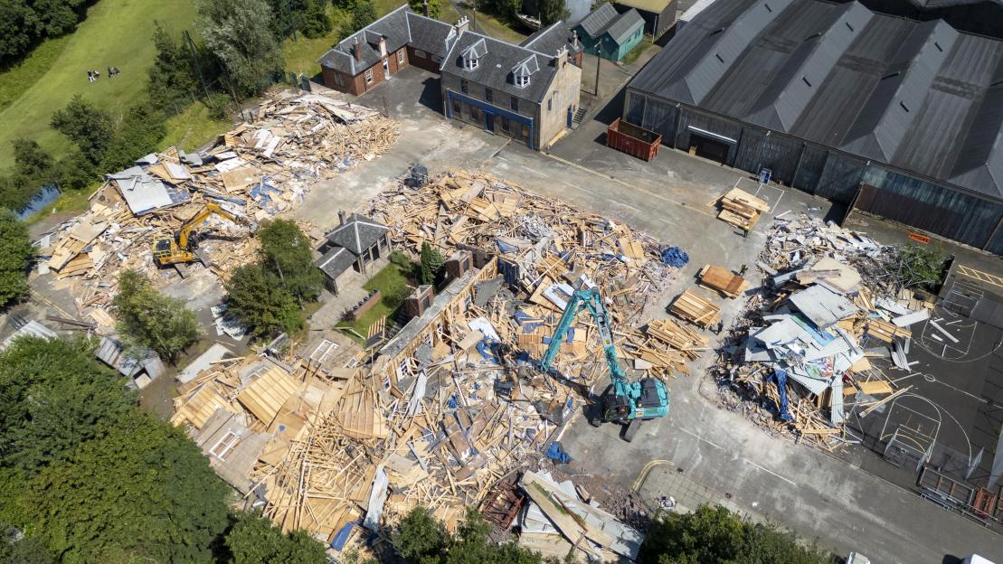 Aerial view of the River City studio set being demolished by two excavators, surrounded by piles of rubble, with some buildings still standing.