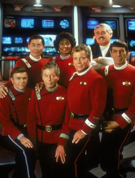 The cast of the film Star Trek VI: The Undiscovered Country posing on the bridge of a starship in red uniforms.