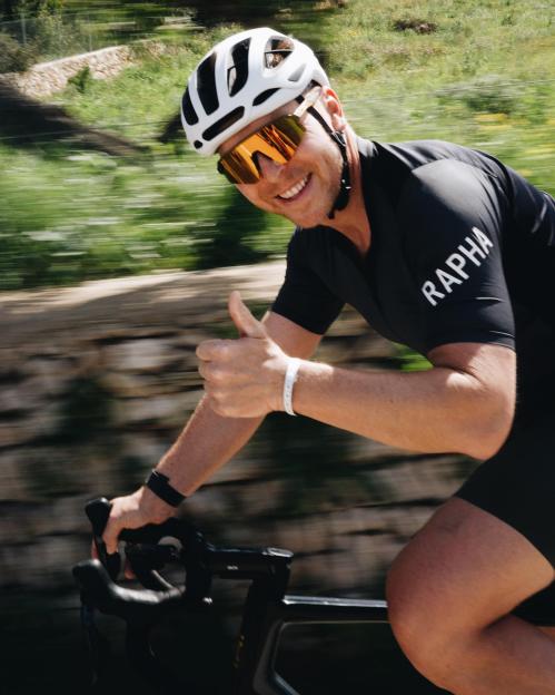 Chris Hoy smiling and giving a thumbs up while cycling in Mallorca.