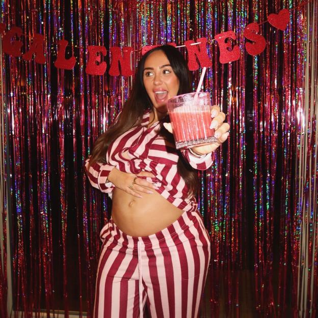 Sophie Kasaei holding a drink, posing in pajamas in front of a sparkly red background with a "VALENTINES" banner.