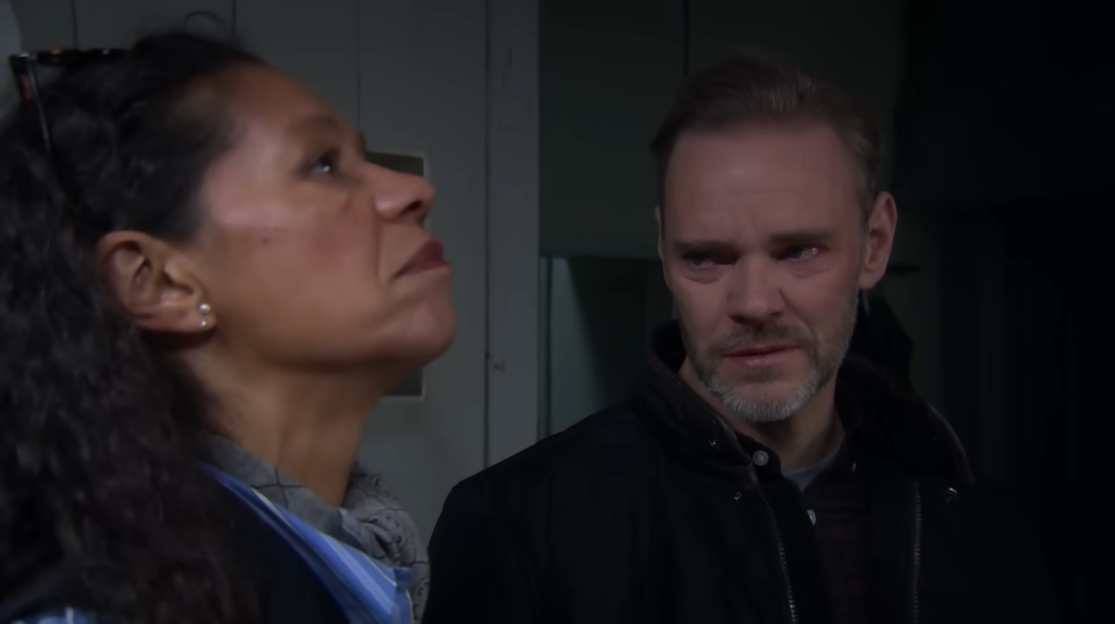 A woman with dark hair looks up and to her right, while a man with a beard and dark jacket looks at her.