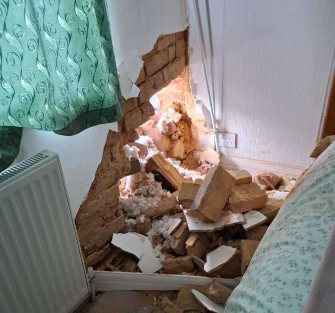 A bedroom wall with a large hole, exposing bricks and insulation, after a car crashed into the house.