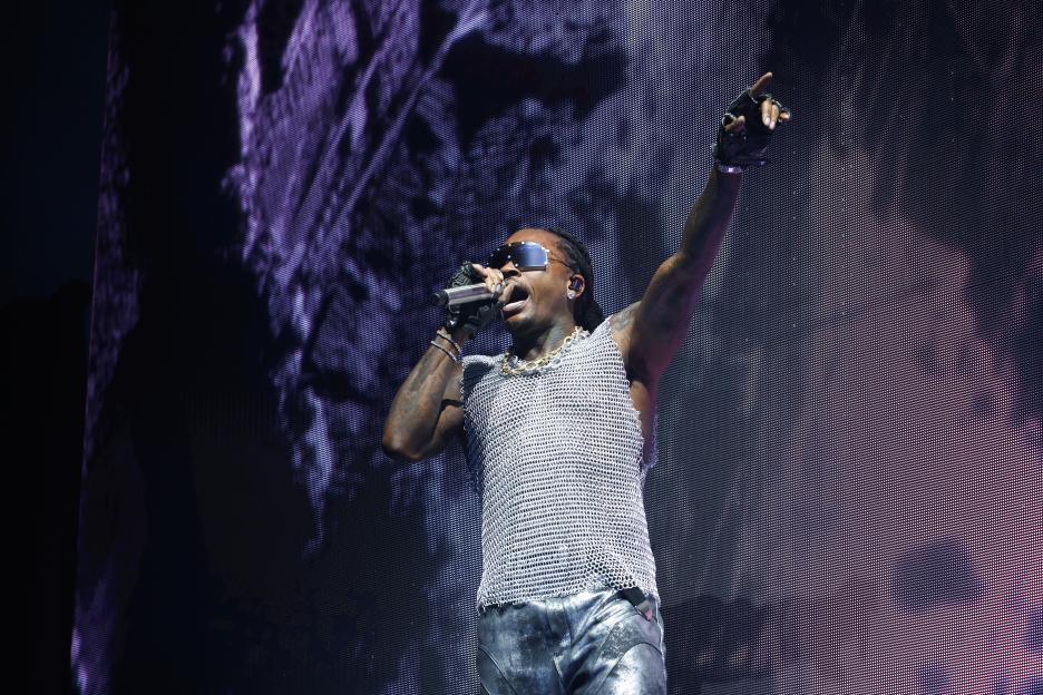 Gunna performs onstage, holding a microphone in one hand and raising the other with a finger pointed.