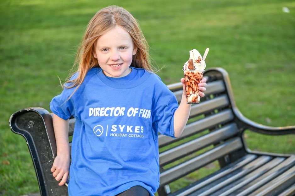 Matilda, aged 10, wearing a "Director of Fun" T-shirt, holds an ice cream while sitting on a park bench.