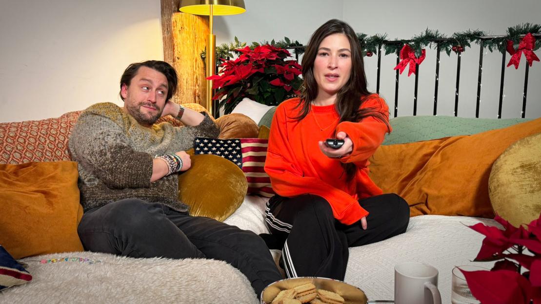 Kieran Culkin and Jazz Charton on a sofa with Christmas decorations, watching TV.