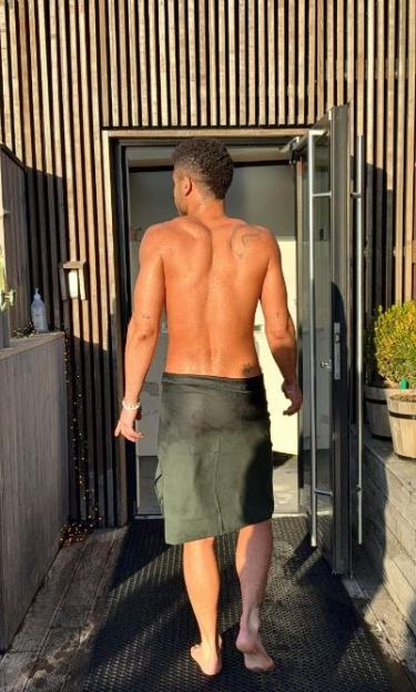 Keye, bare-chested and wearing a towel, walks towards an open door.