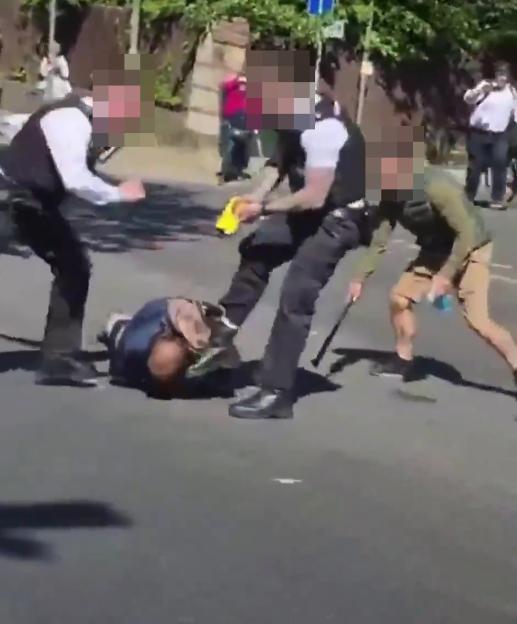 Police detaining a suspect on the ground with two officers standing over him and a third nearby.