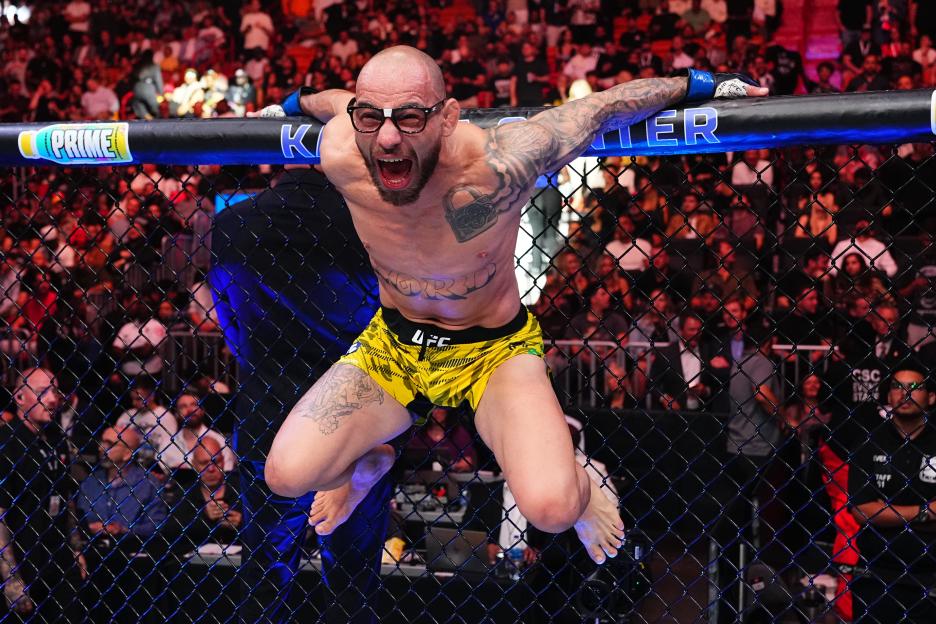 UFC fighter Baldy Silva wearing glasses and pointing to them while holding a microphone.