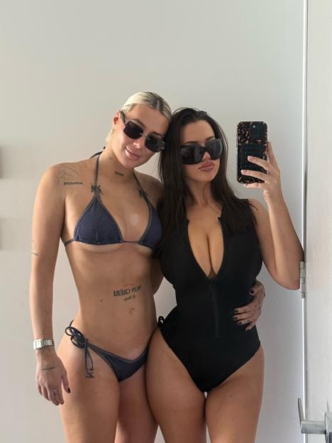 Gabby McCarthy in a bikini and Demi Sims in a black swimsuit, both wearing sunglasses and posing for a mirror selfie.