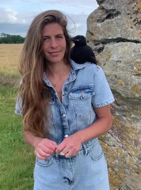 Hannah Bourne-Taylor standing with a black bird on her shoulder.