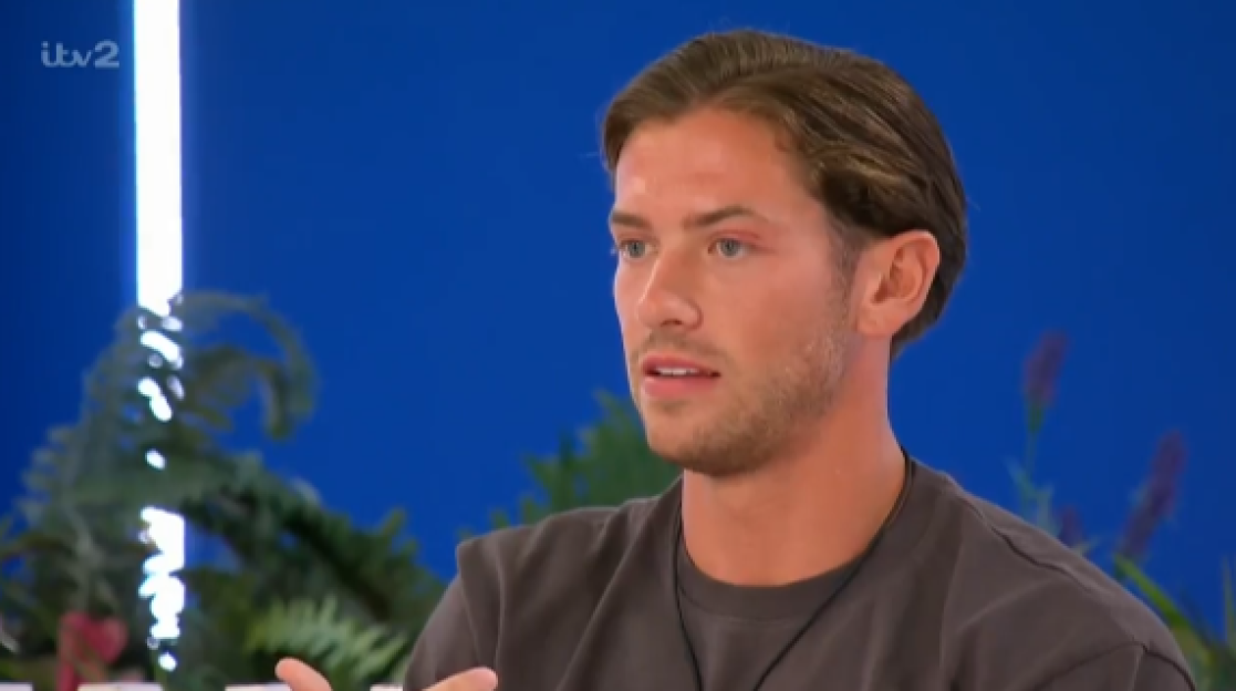 Man with light brown hair and a dark shirt looking slightly to the right with his mouth open, as if speaking.