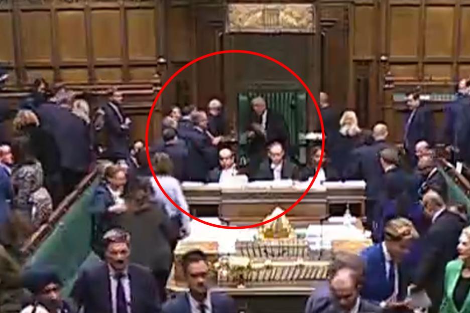 A red circle highlights a group of people standing and talking in a government chamber.