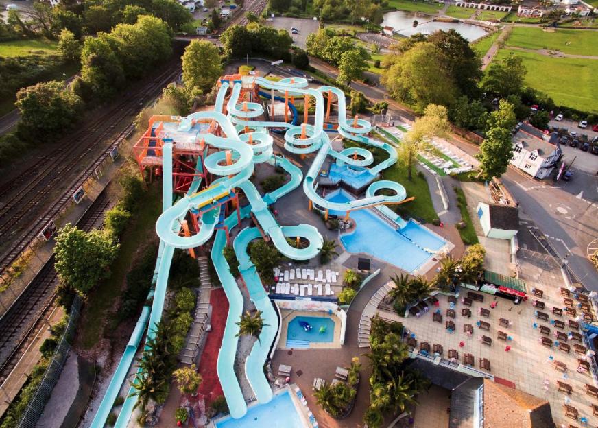 Aerial view of Splashdown Quaywest waterpark, with numerous light blue water slides and pools, next to a railway line and green areas.