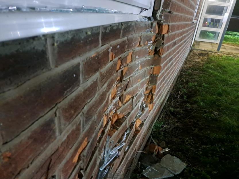 Damaged brick wall with broken window glass and exposed bricks.