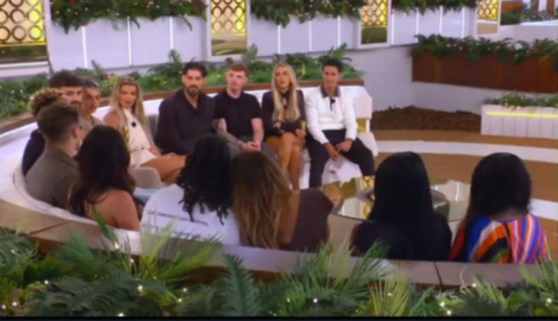 Several contestants on Love Island sit in a curved seating area.