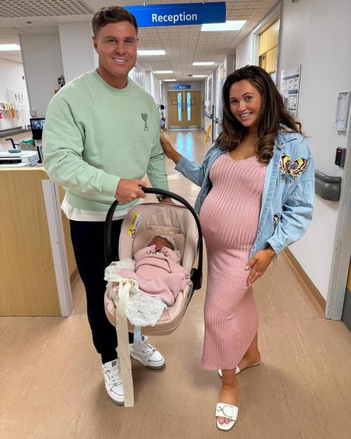 Charlotte Dawson and her partner in a hospital hallway with their newborn baby daughter in a car seat.