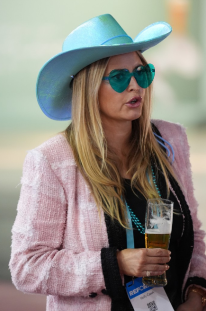 Woman in a blue cowboy hat and heart-shaped sunglasses, holding a glass of beer.