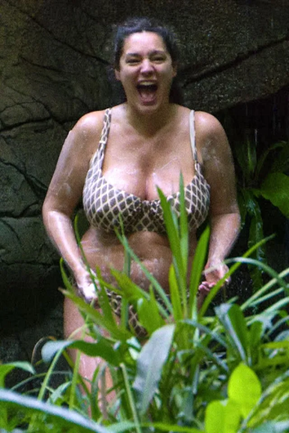 A woman in a patterned bikini screams with laughter in a jungle shower.