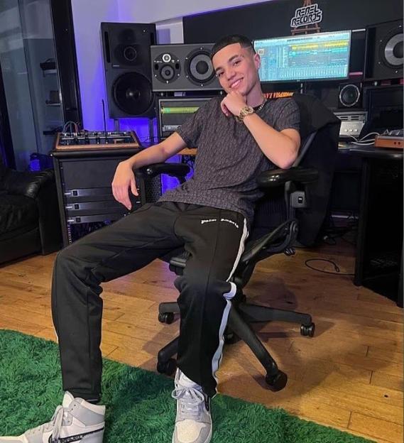 A young man in a recording studio smiles while sitting in a chair.