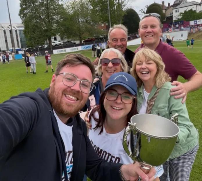 Group of people celebrating on a playing field with a trophy.