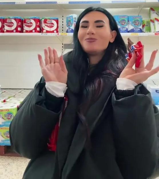 Brittany Miller holding an unwrapped candy bar in a supermarket aisle.