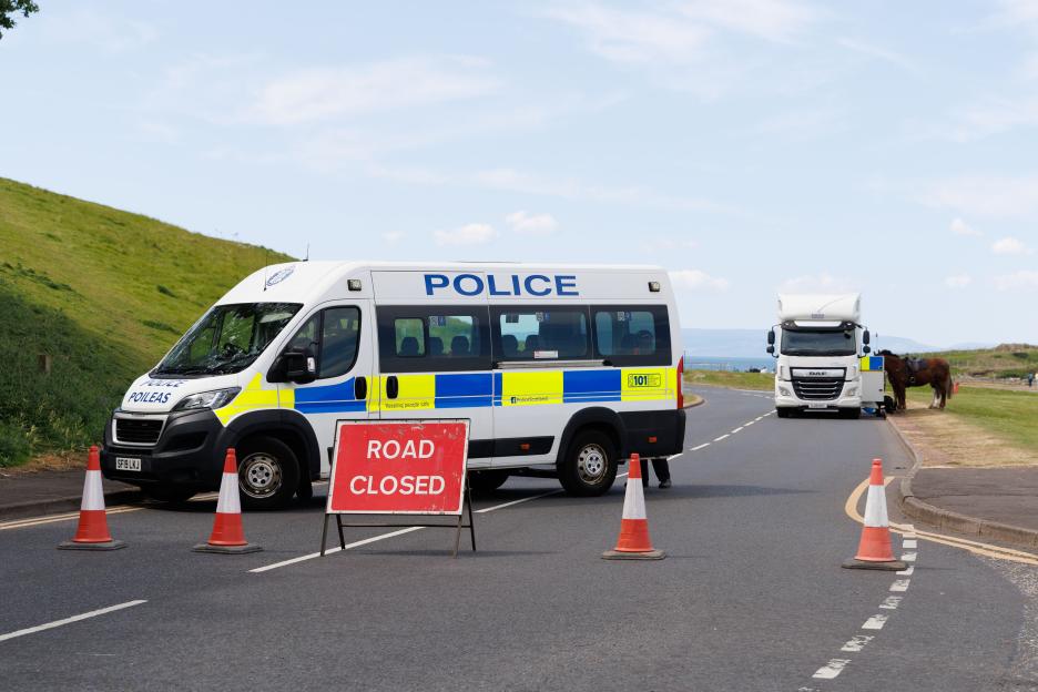 Police van and "ROAD CLOSED" sign at Irvine Beach after a serious incident.