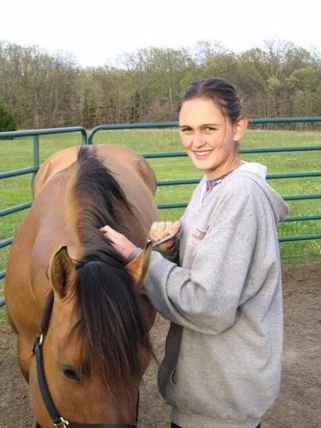 A young woman grooming a brown horse.