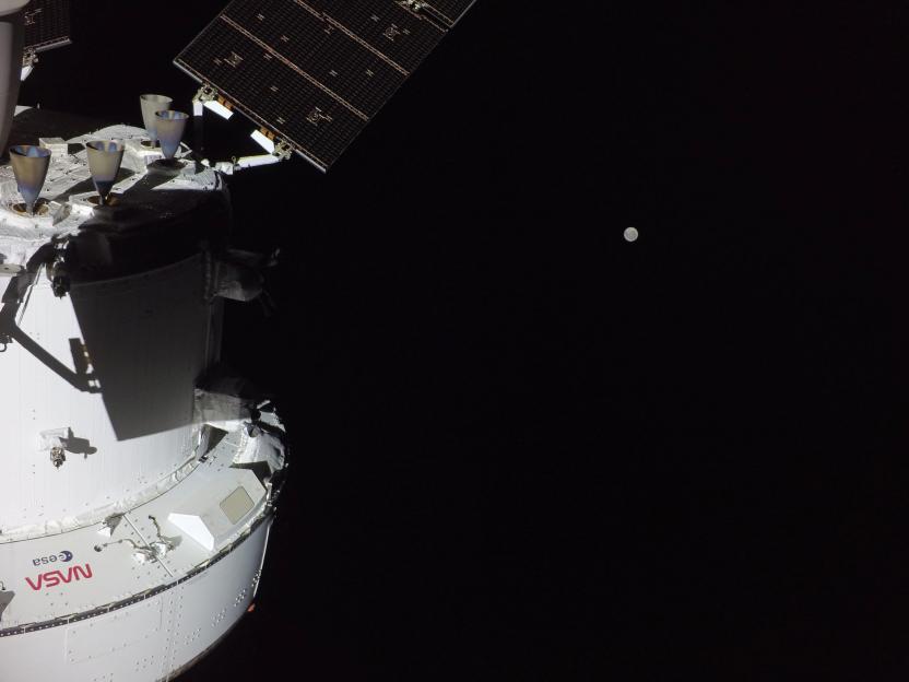 The Orion capsule and its solar array in outer space with the Moon visible in the distance.