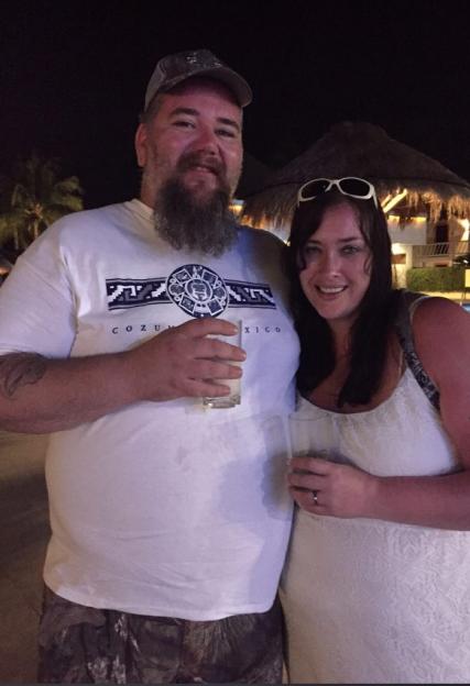 A man and a woman stand together at night, both holding glasses.