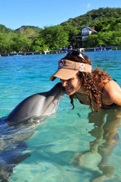Ingrid Honkala, wearing a visor, interacts with a dolphin in clear blue water.