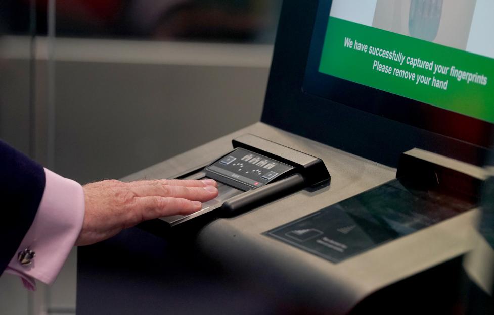 A person uses a fingerprint scanner on a terminal that reads "We have successfully captured your fingerprints. Please remove your hand."