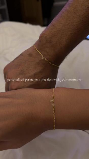 Two people wearing matching gold chain bracelets on their wrists.