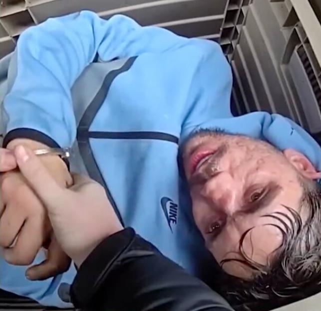 A man in a blue sweatshirt is apprehended and handcuffed inside a garden box.