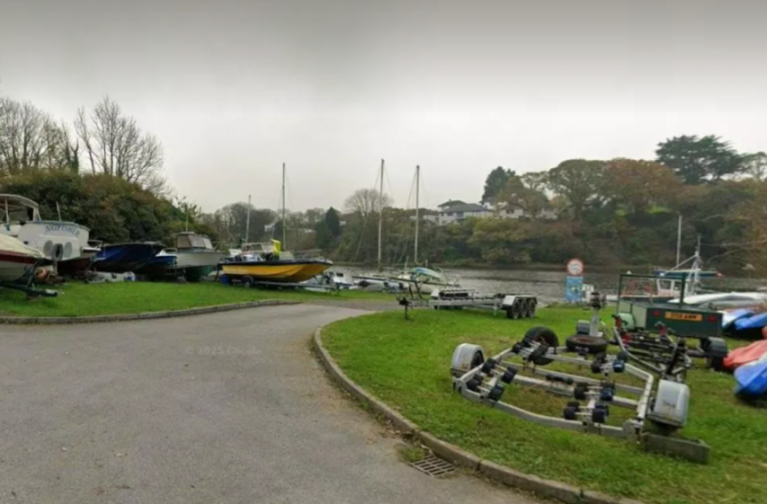 Boats and trailers on a grassy embankment next to a body of water.
