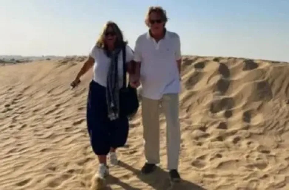 A man and a woman walk hand-in-hand across sandy dunes under a clear blue sky.