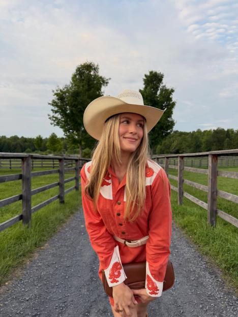 Genie Bouchard posing in a red cowgirl outfit and cowboy hat on a gravel road.