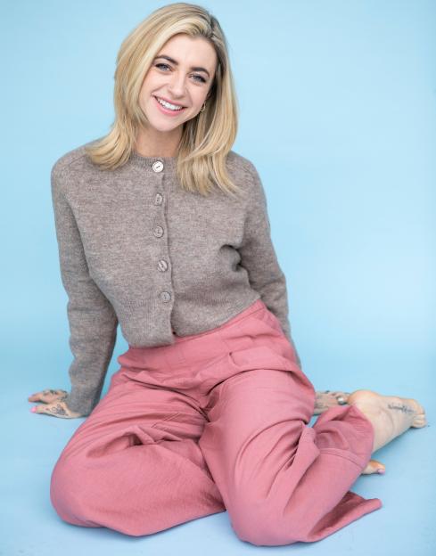Saurora Grace, a 31-year-old sex surrogate, smiling while sitting in a beige sweater and pink pants.